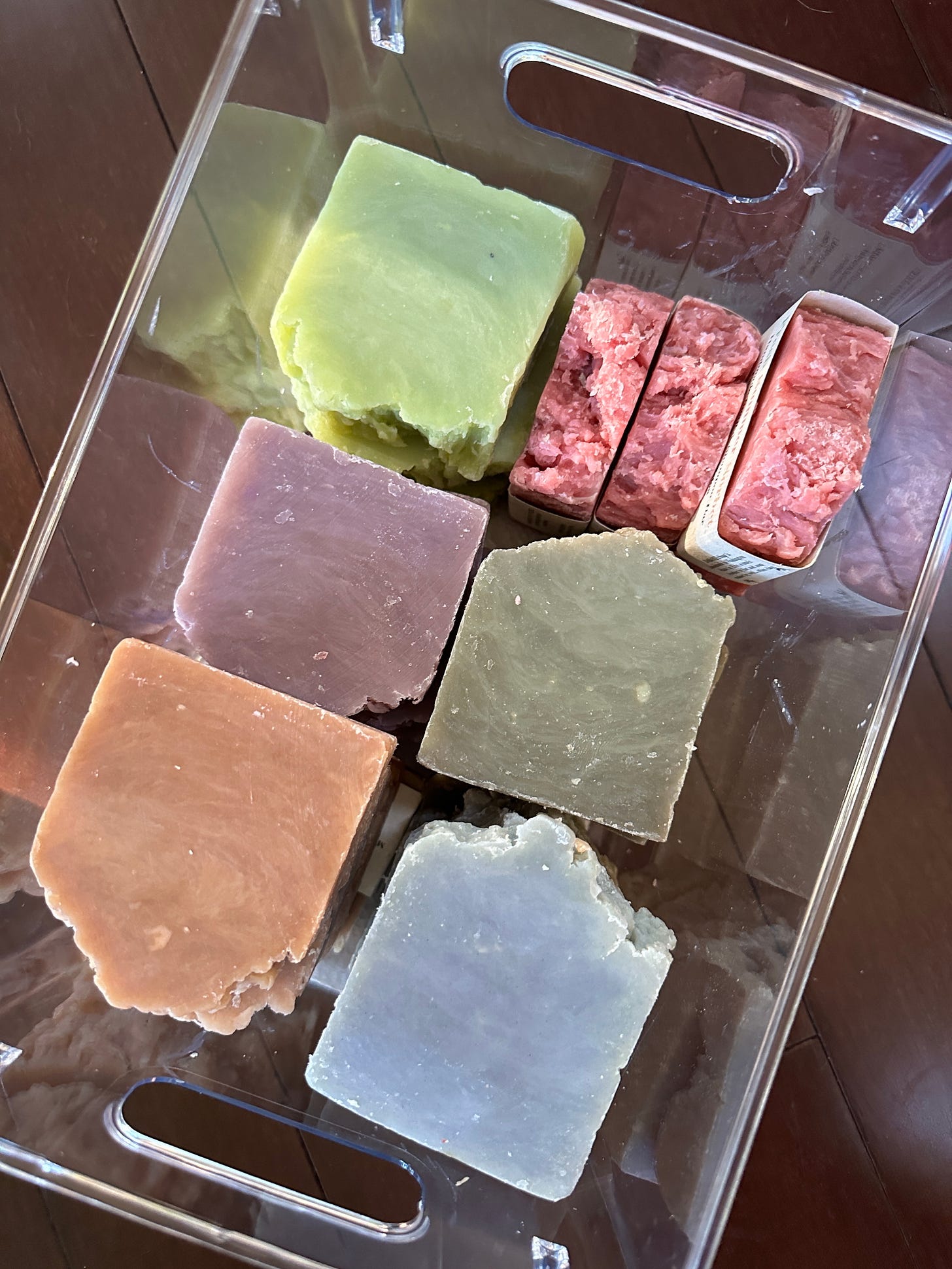 A clear storage container with bars of handmade soap in various colors.