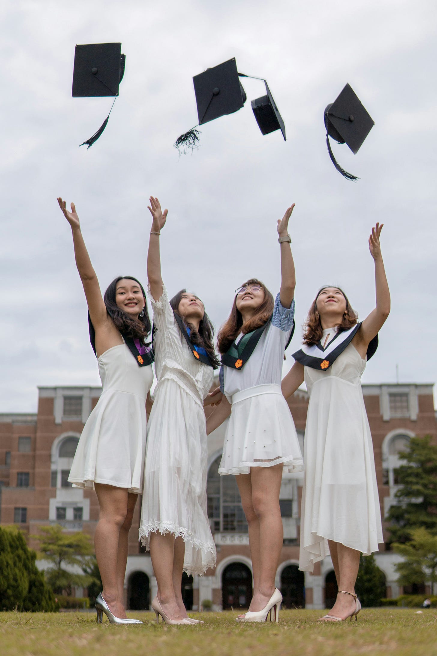 Four girls, dressed in white, throwing graduation gowns in the air