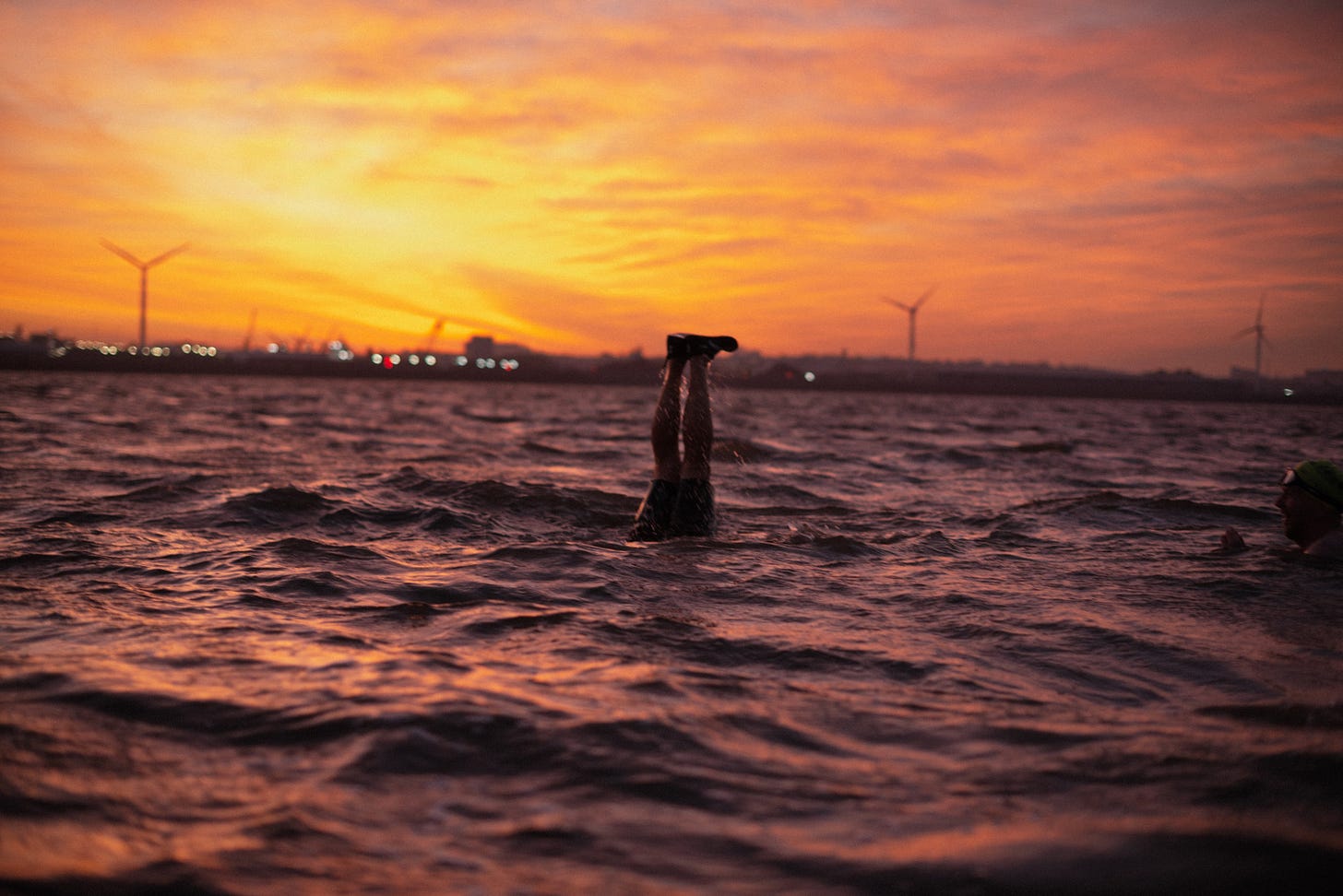 A man does a handstand in the River Mersey at sunrise. Only his legs are visible.