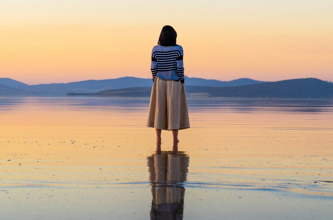 woman in black and white dress standing on beach during sunset