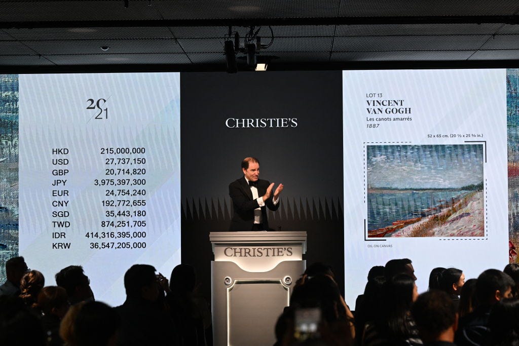 A man stands on a rostrum during an auction in front of two digital screens. A man stands on a rostrum during an auction in front of two digital screens.