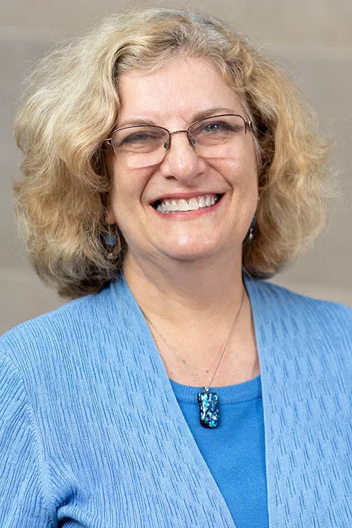 A woman wears a blue shirt and smiles into the camera.