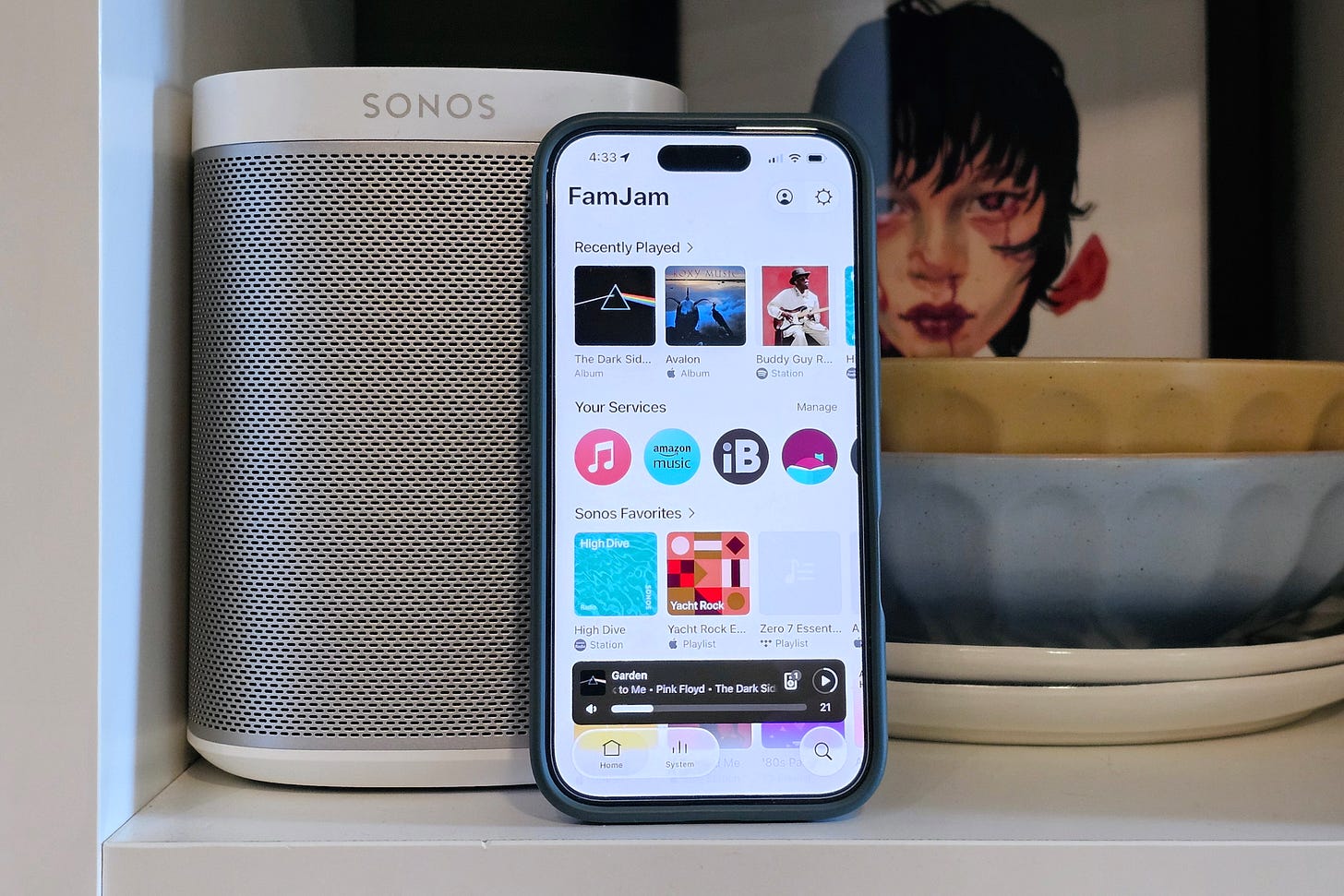 An iPhone showing the home screen of the newly redesigned Sonos app, sitting next to a white Sonos Play:1 speaker. An iPhone showing the home screen of the newly redesigned Sonos app, sitting next to a white Sonos Play:1 speaker.
