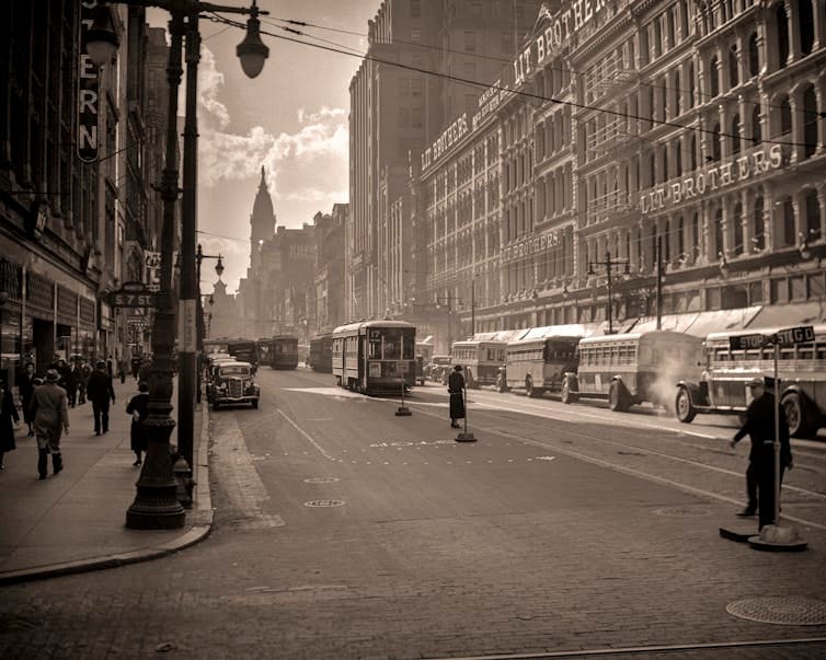 Sepia-toned photo of busy street in a commercial area of a city circa 1930s