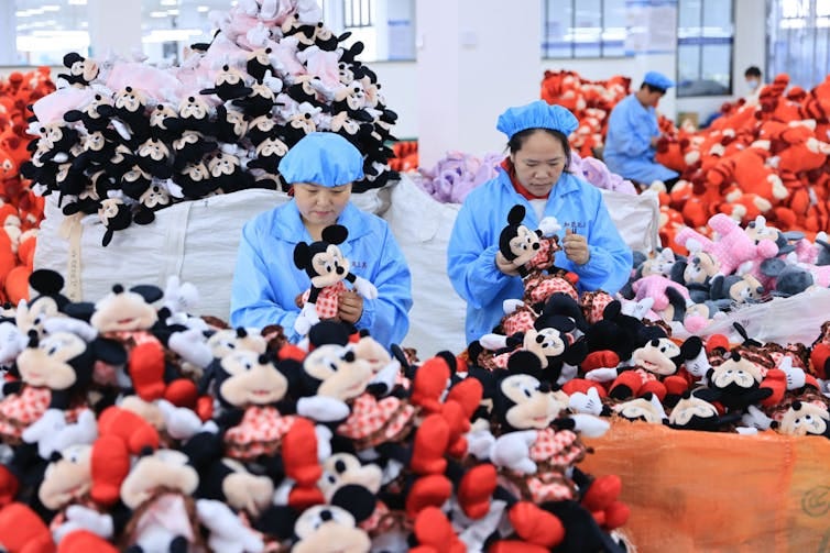 Two female workers wearing blue surrounded by piles of stuffed animals. Two female workers wearing blue surrounded by piles of stuffed animals.