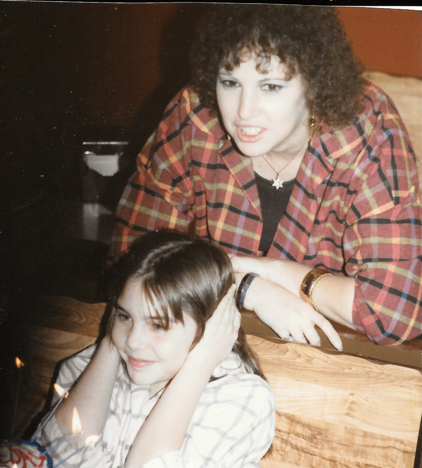 Mid-80s photo of mom, smiling behind me; I'm covering my ears, and there's a lit birthday cake in front of me
