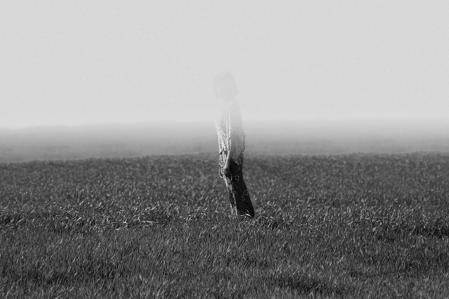 black and white of a man standing in a field but half of him has faded almost to trasnparent