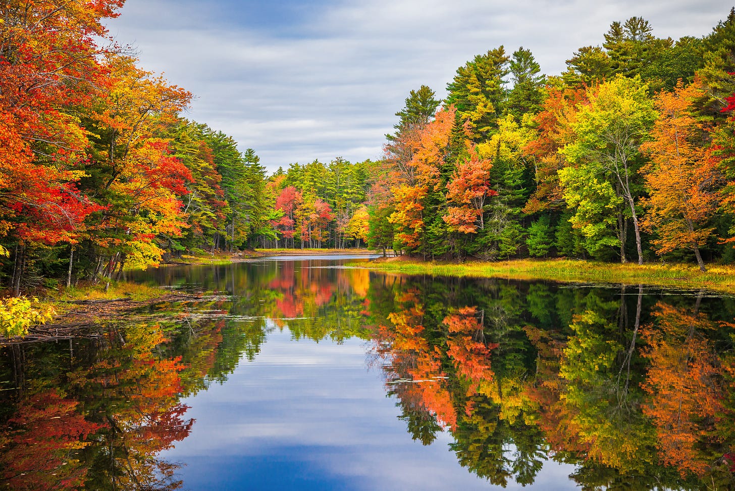 Trees with fall leaves on both sides of a lake with the colors of leaves reflected in the smooth surface of the lake