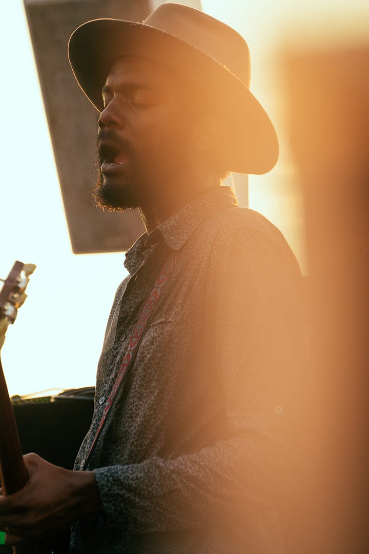 A collage of five photos of Gary Clark Jr. performing outdoors. The images are a mix of color and black and white, featuring close-ups of his face as he sings and wider shots of him playing the guitar, all while wearing his signature hat.
