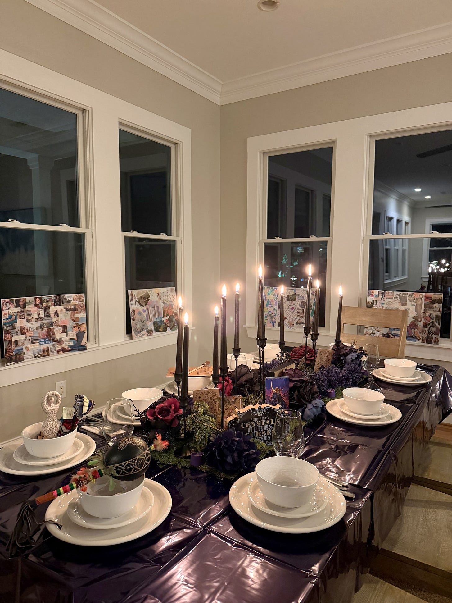A candlelit retreat dinner table with black taper candles, deep purple florals, and white place settings.