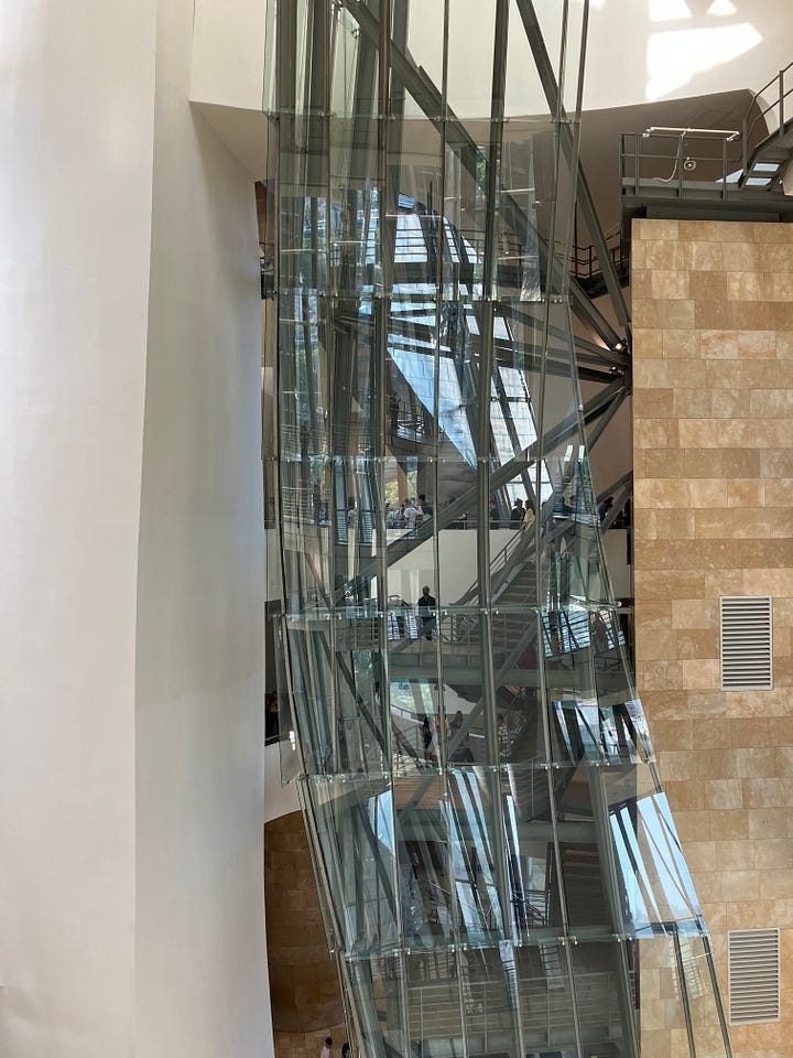 a view of spiral metal sculptures from above, with people around and within them, and a view through splintered glass of an elevator shaft