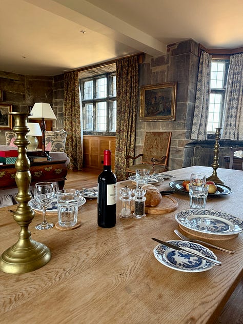 Images show armchairs before a wood burning stove with a dog sprawled on the carpet; a balustrade and domed octagonal tower on a stone roof; and a table set with plates, candlesticks, wine and bread on an oak table