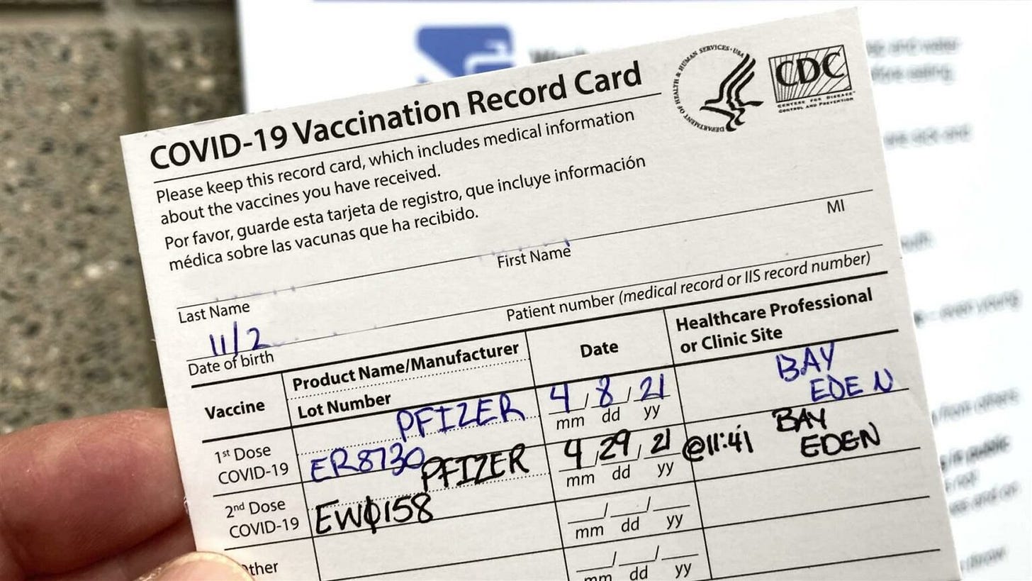  hand holding a handwritten CDC COVID-19 Vaccination Record Card showing two Pfizer doses from April 2021.