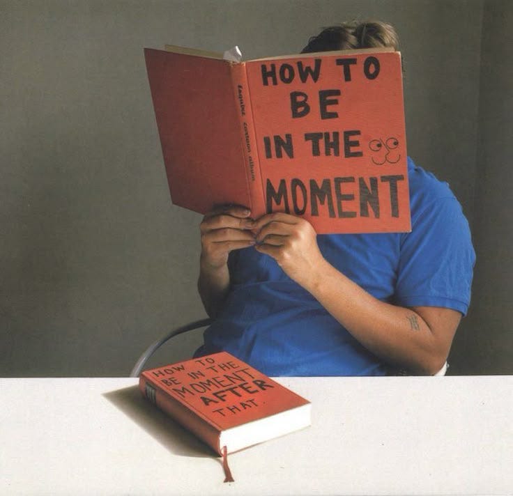 This may contain: a person sitting at a table with a book over their head and the words how to be in the moment written on it