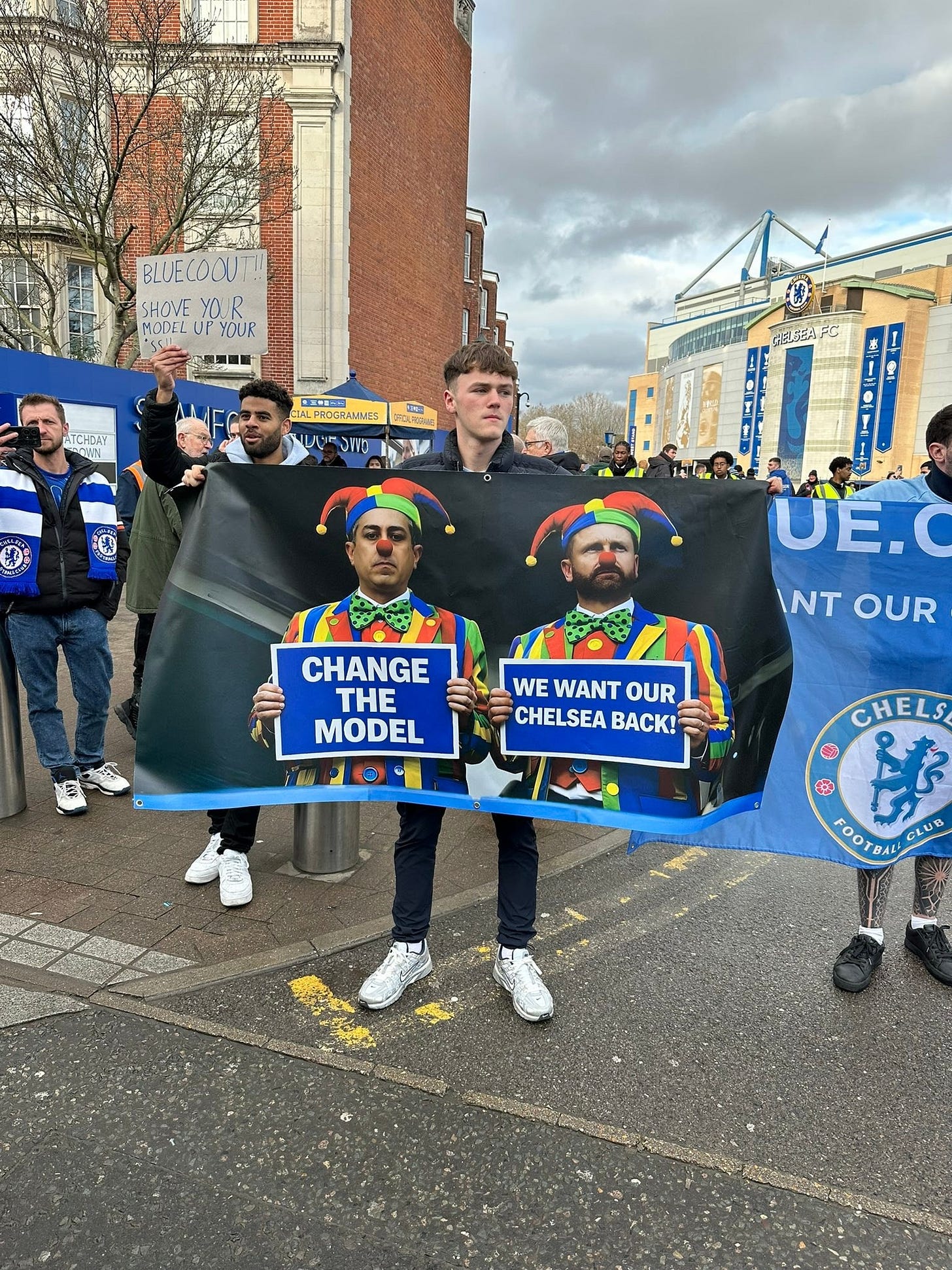 可能是‎顯示的文字是「 ‎BLUECOOUT! SHOVE YOUR MODFL UP YOUR TCHOAY AYYAN 대제 音者 FROGRANNES משוהצש ህላዊ DAVD FELTEAFC UE. INTOUR INT OUR CHANGE THE MODEL WE WANT OUR CHELSEA BACK! CHELS S $ កំ FOOTB OOT6ли.ασю CLUB‎ 」‎的圖像