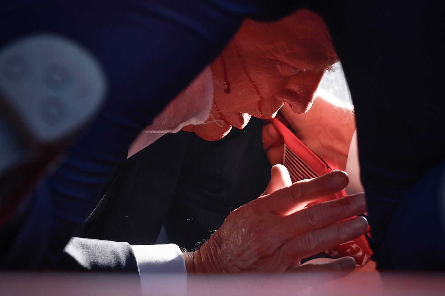 Trump covered by Secret Service agents, with blood lines running across his face.