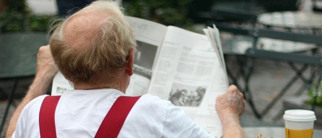 a man sitting at a table reading a newspaper