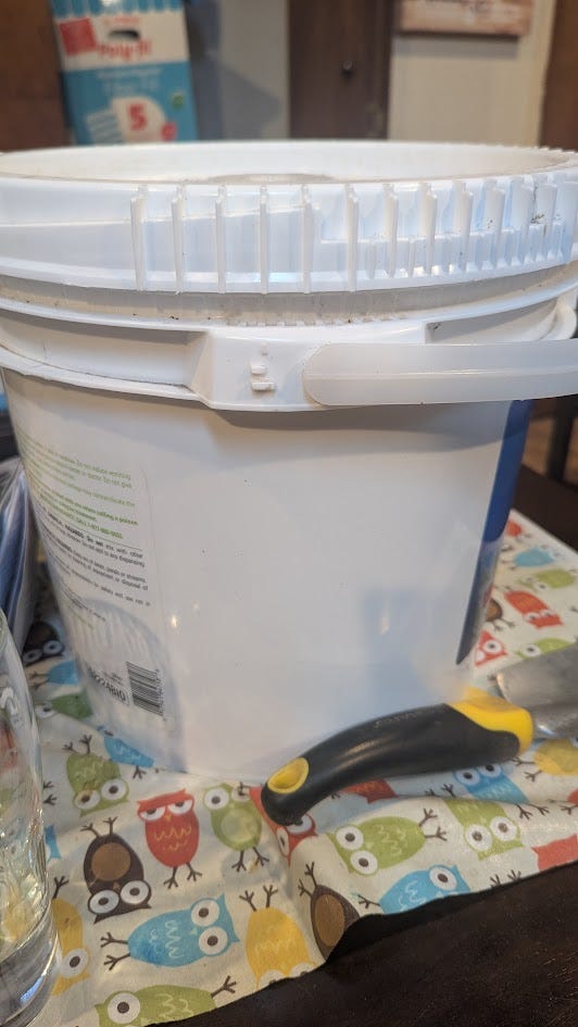 A white plastic bucket with a lid, the inside contains many seed packets in plastic bags.