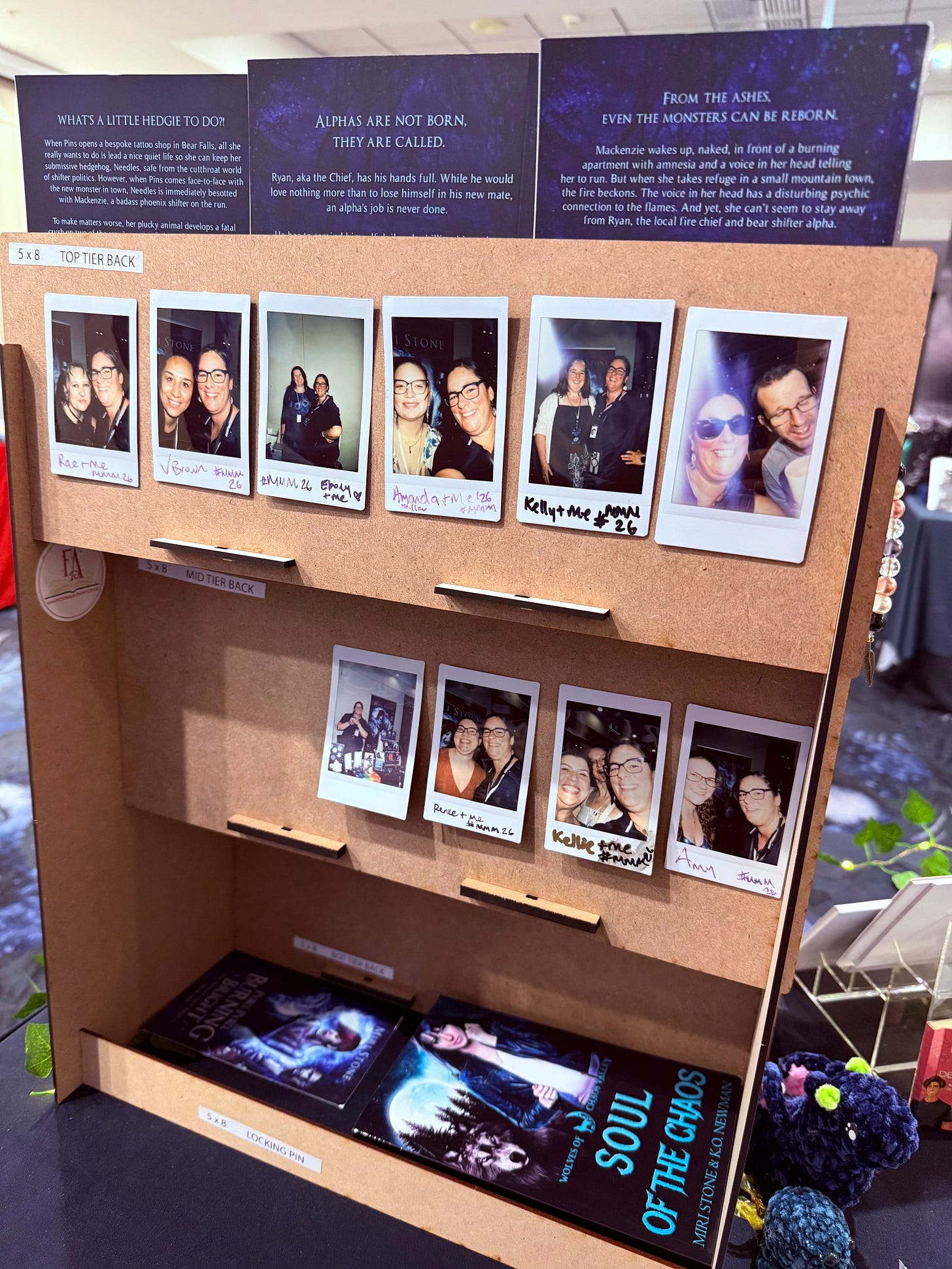 Behind the scenes: the back of Miri Stone's book stand at Meet Me in the Mountains where polaroids are stuck to the back showing her with friends and readers from the signing
