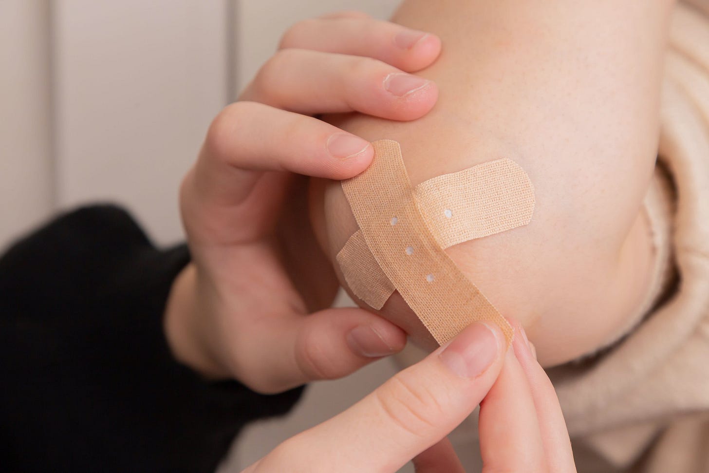 Photograph of a person applying bandaids to someone else's elbow. Photograph of a person applying bandaids to someone else's elbow.