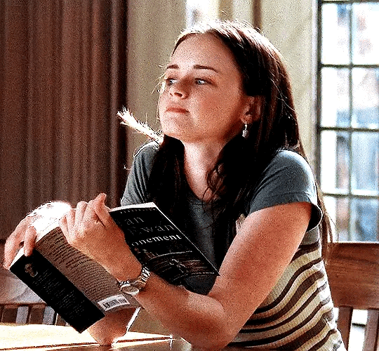This may contain: a woman sitting at a table with an open book in her hand and looking up