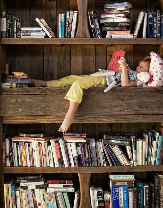 This may contain: a young boy laying on top of a book shelf filled with books