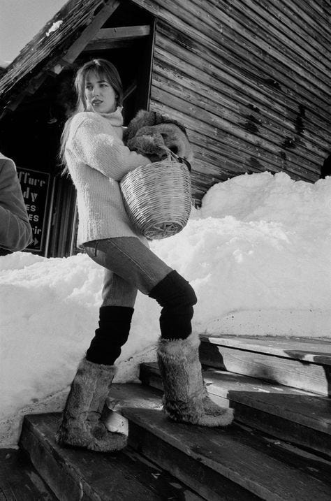 This may contain: black and white photograph of a woman holding a teddy bear in front of a cabin