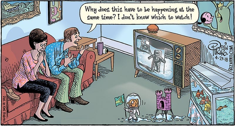 Comic of a couple watching the 1969 moon landing on TV, as fish in an aquarium nearby watch as one of their fellow fish has landed on the carpet in front of the TV, wearing an astronaut suit, holding a flag with a fish tail on it. He seems to have traveled there in the pink, miniature castle typical of home aquariums. The humans on the couch are amazed, one saying, “Why does this have to be happening at the same time? I don’t know which to watch!”