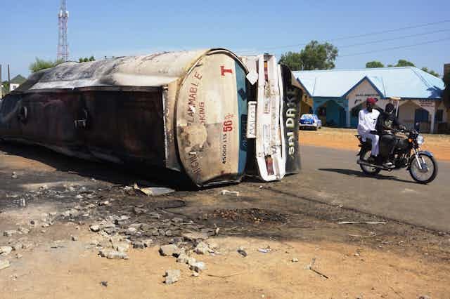 Fuel tanker lying on its side; motorcycle passes Fuel tanker lying on its side; motorcycle passes