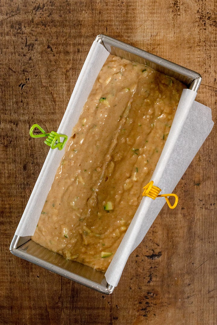 Two images of zucchini bread batter, one in a glass bowl with a green spatula and the other with the batter in a prepared loaf pan lined with parchment paper.