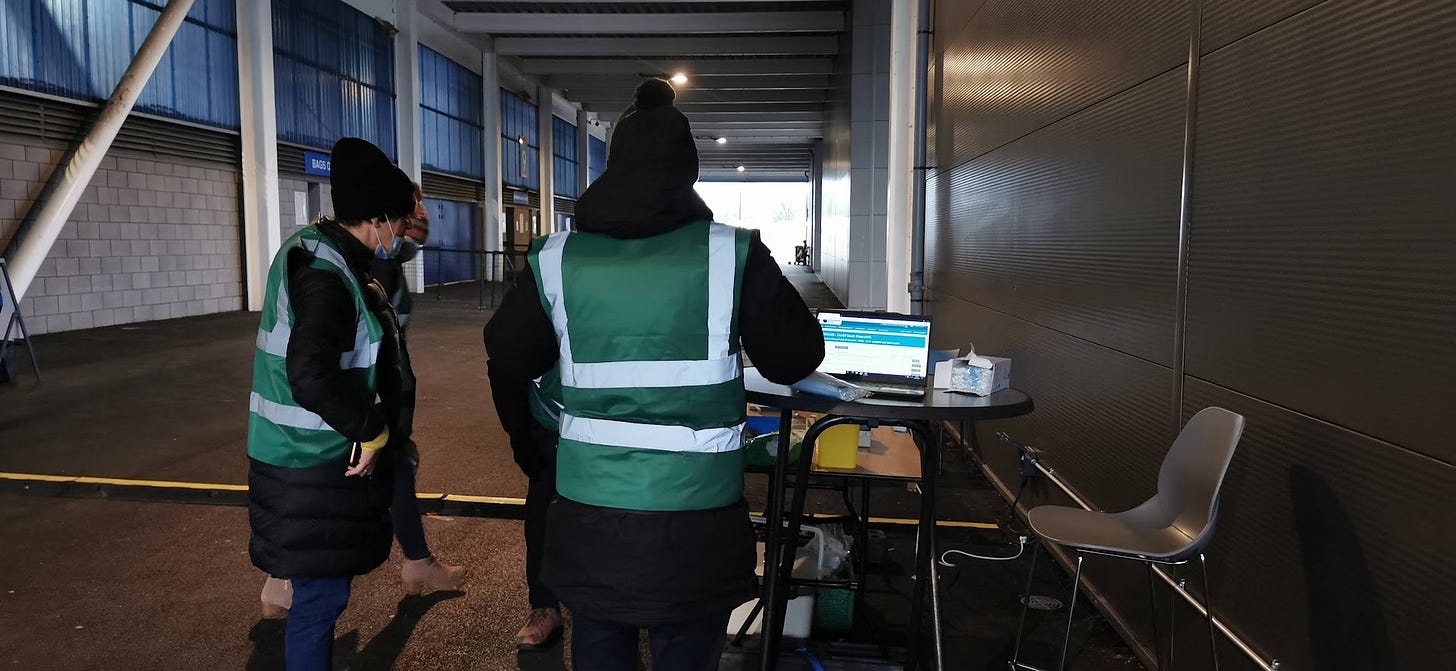 A tunnel behind Cardiff City Stadium where a drive-through vaccination centre was set up in January 2021. Several people in high vis tabbards and hats stand around a laptop. 