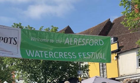 Picnic hamper filled with dozens of watercress & cheese scones; a Hey Duggee balloon looking especially happy above a stall selling watercress-inspired burgers, and the festival banner against a blue sky.