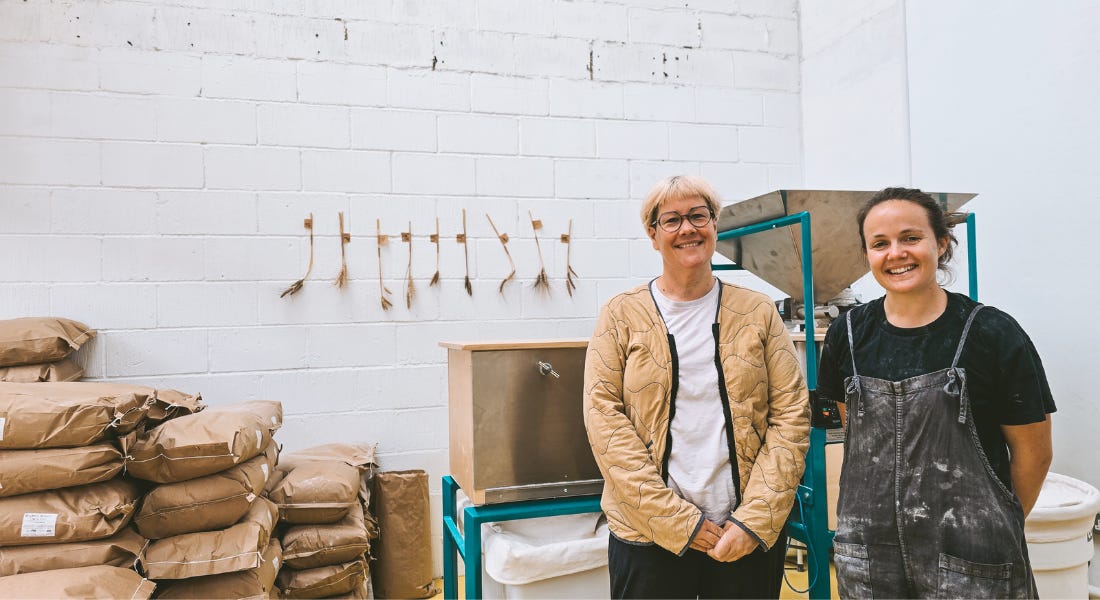 Kim Bell and Emma Shires standing in front of a milling machine, with bags of flour to the left of them