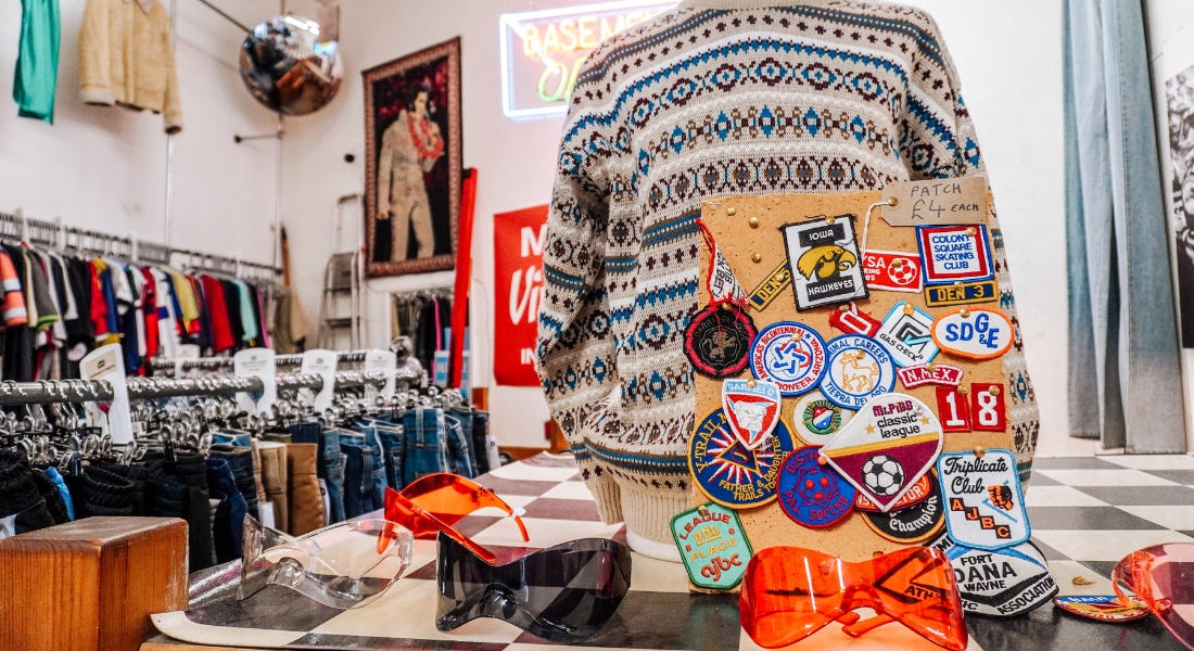 A shop interior with a stand with sunglasses and a jumper on it, with clothes rails in the background