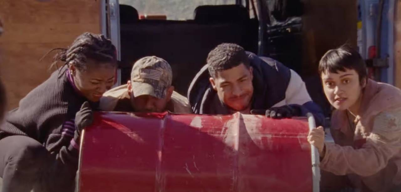 Four people grimace as they attempt to push a heavy red barrel. Four people grimace as they attempt to push a heavy red barrel.