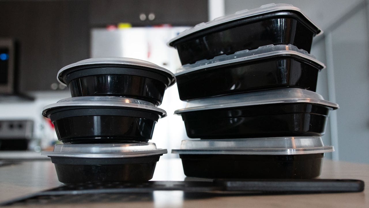 A stack of black plastic takeout containers with a black plastic spatula in the foreground. A stack of black plastic takeout containers with a black plastic spatula in the foreground.