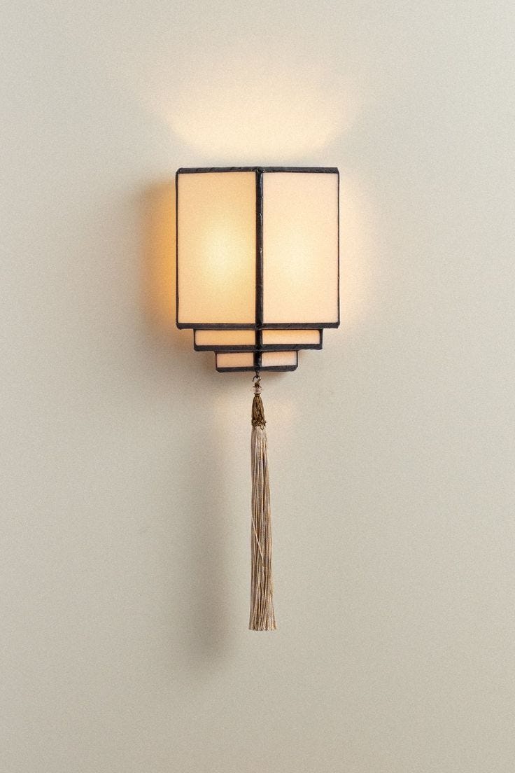 This may contain: a wall light with a tassel hanging from it's side against a white wall