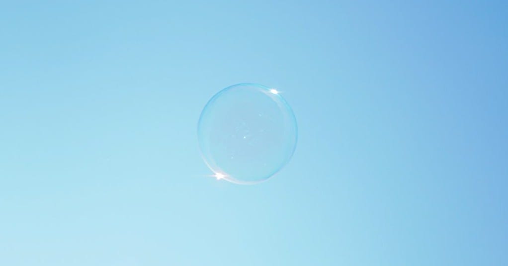 A soap bubble floats against a blue sky.