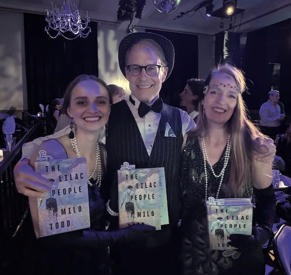 Julie Carrick Dalton with her husband and daughter, all three dressed in Roaring Twenties attire and holding copies of Milo Todd's novel The Lilac People.