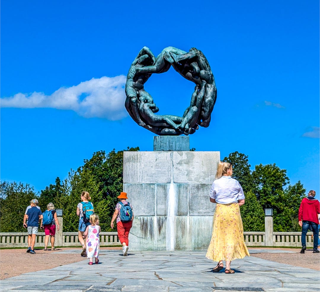 A woman in a yellow dress is right in front of the sculpture, children and other people nearby. 