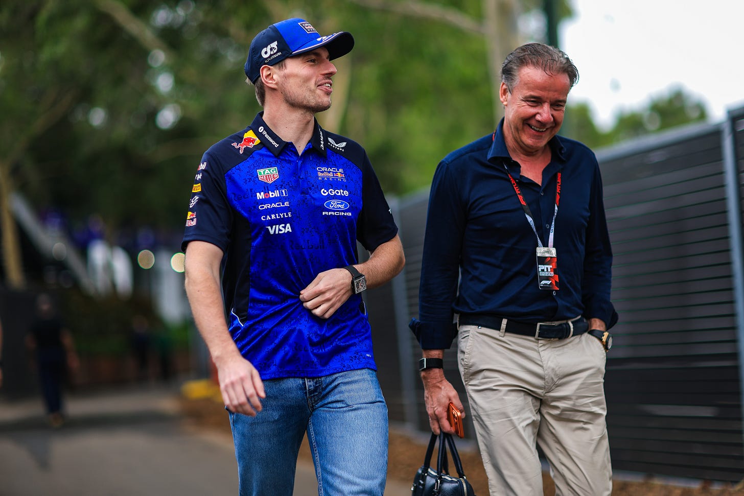 Max Verstappen and Raymond Vermeulen laughing as they talk while walking in the F1 paddock