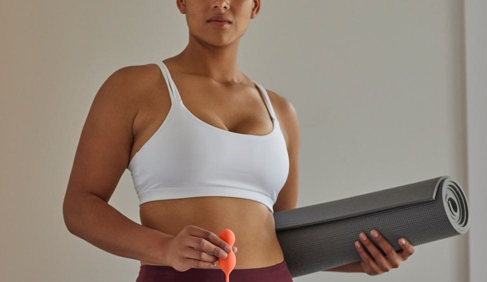 woman in white sports bra and purple leggings holding black speaker