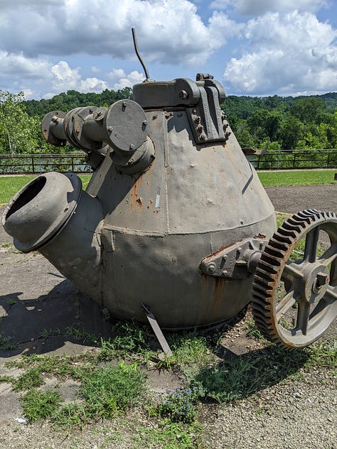 The remains of a massive 12,000 ton press now a rusting frame standing outdoors behind a chain-link fence on a bright blue day.