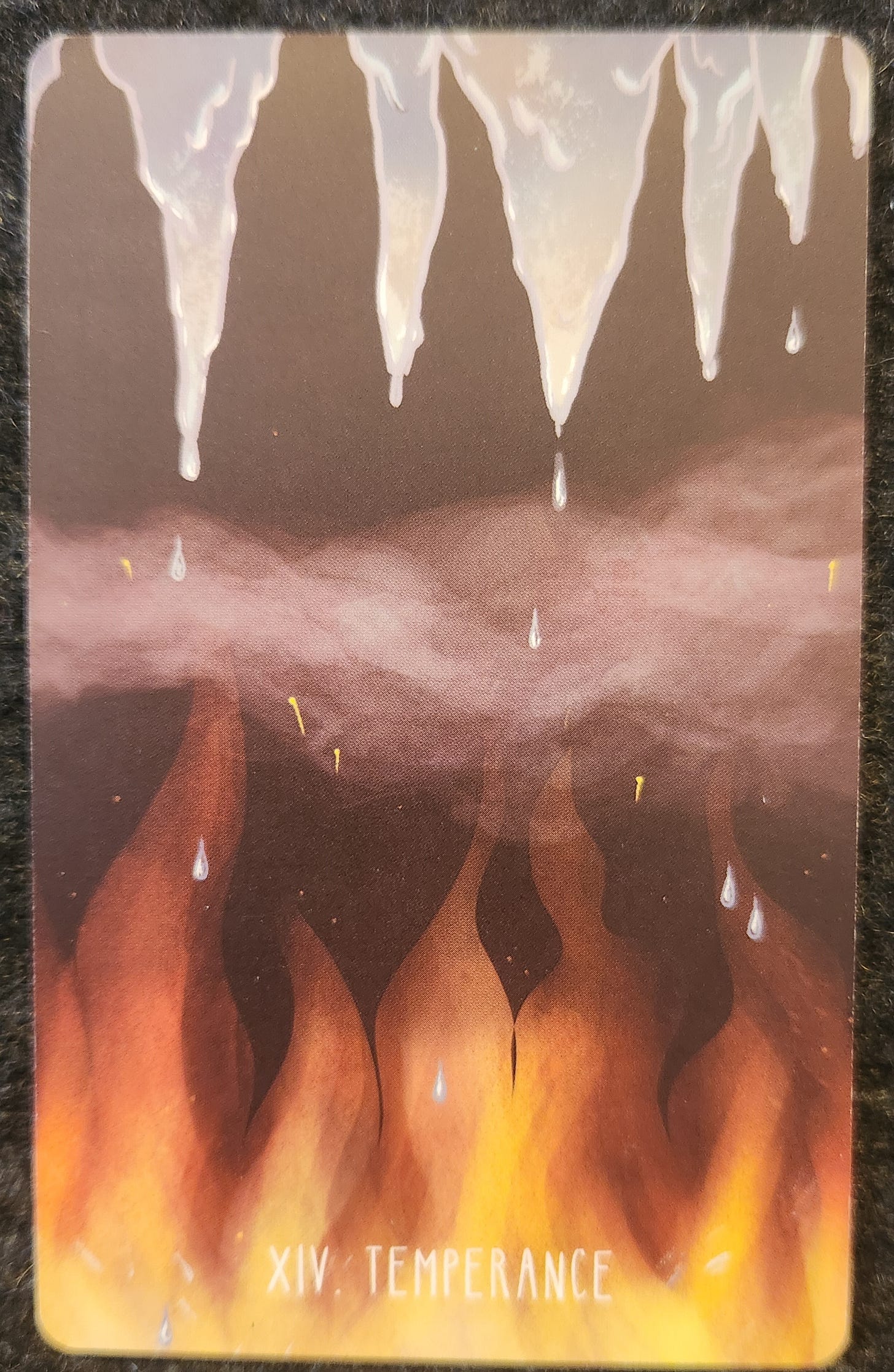 A tarot card labelled XIV. Temperance. The card shows a row of icicles hanging from the top over a row of tall yellow, orange, and red flames. The icicles are melting into the fire. A swirl of steam or mist moves between the ice and fire. 