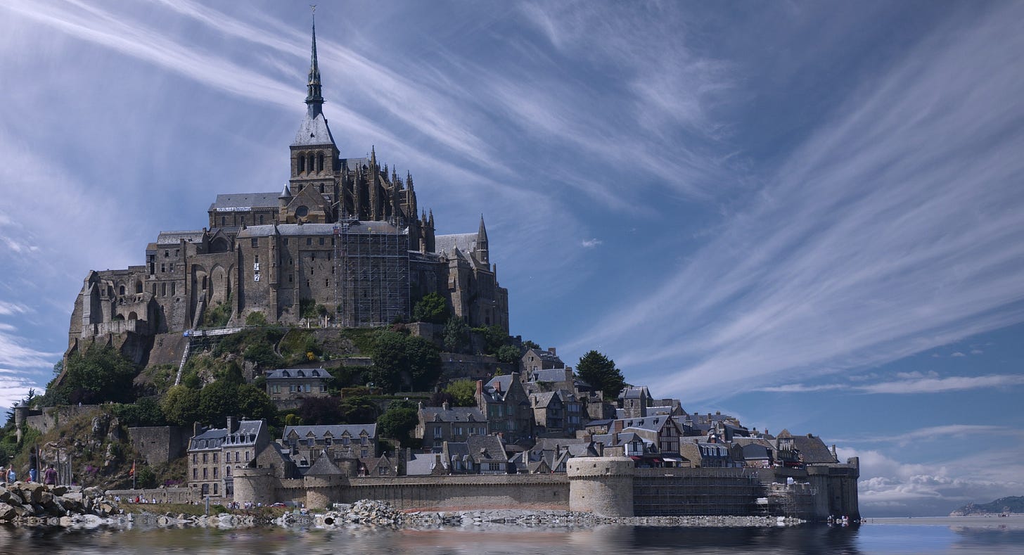 A castle high above the water, surrounded by smaller houses and a wall