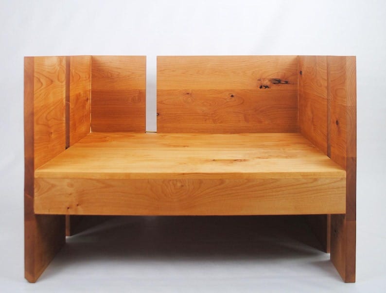 May include: A wooden bench with a light brown finish. The bench is made of multiple pieces of wood that are joined together to form a rectangular shape. The bench has a simple design and is made of natural wood.
