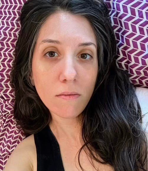 selfie of me lying in bed. my facial expression is unhappy, and I look tired and pale.