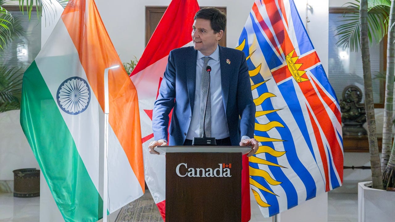 A tall man stands at a podium marked 'Canada' in front of flags of India, Canada and B.C.