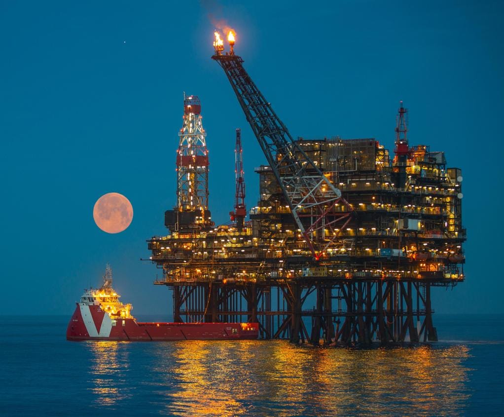 North Sea oil platform at night with flare and supply vessel.