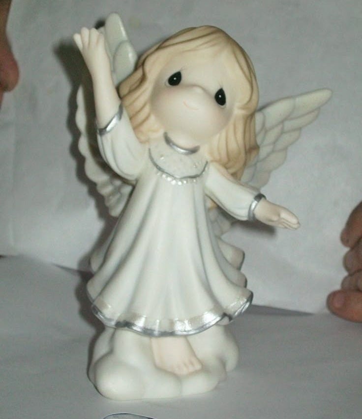 This may contain: a white angel figurine sitting on top of a table next to a piece of paper